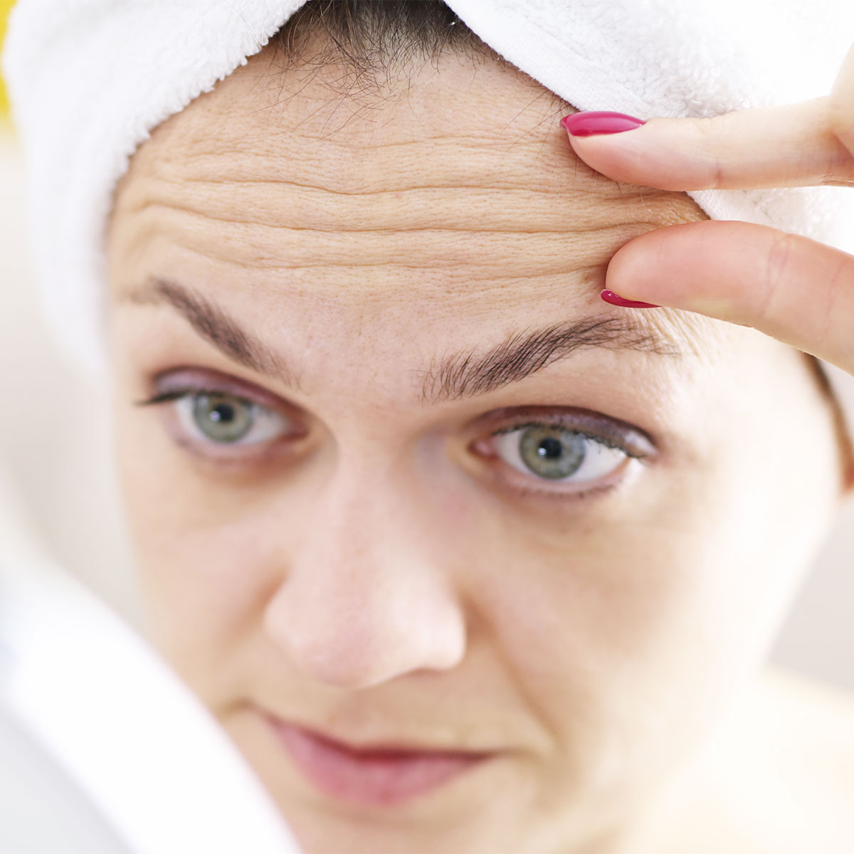 woman looking at forehead wrinkles in mirror white turban