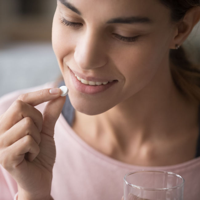 woman taking supplement with glass of water
