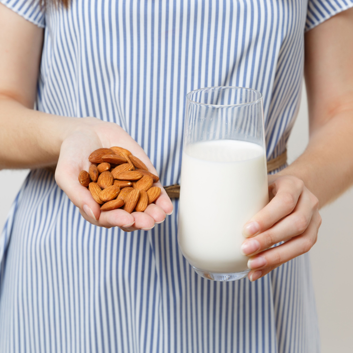 woman holding glass of almond milk and handful of almonds