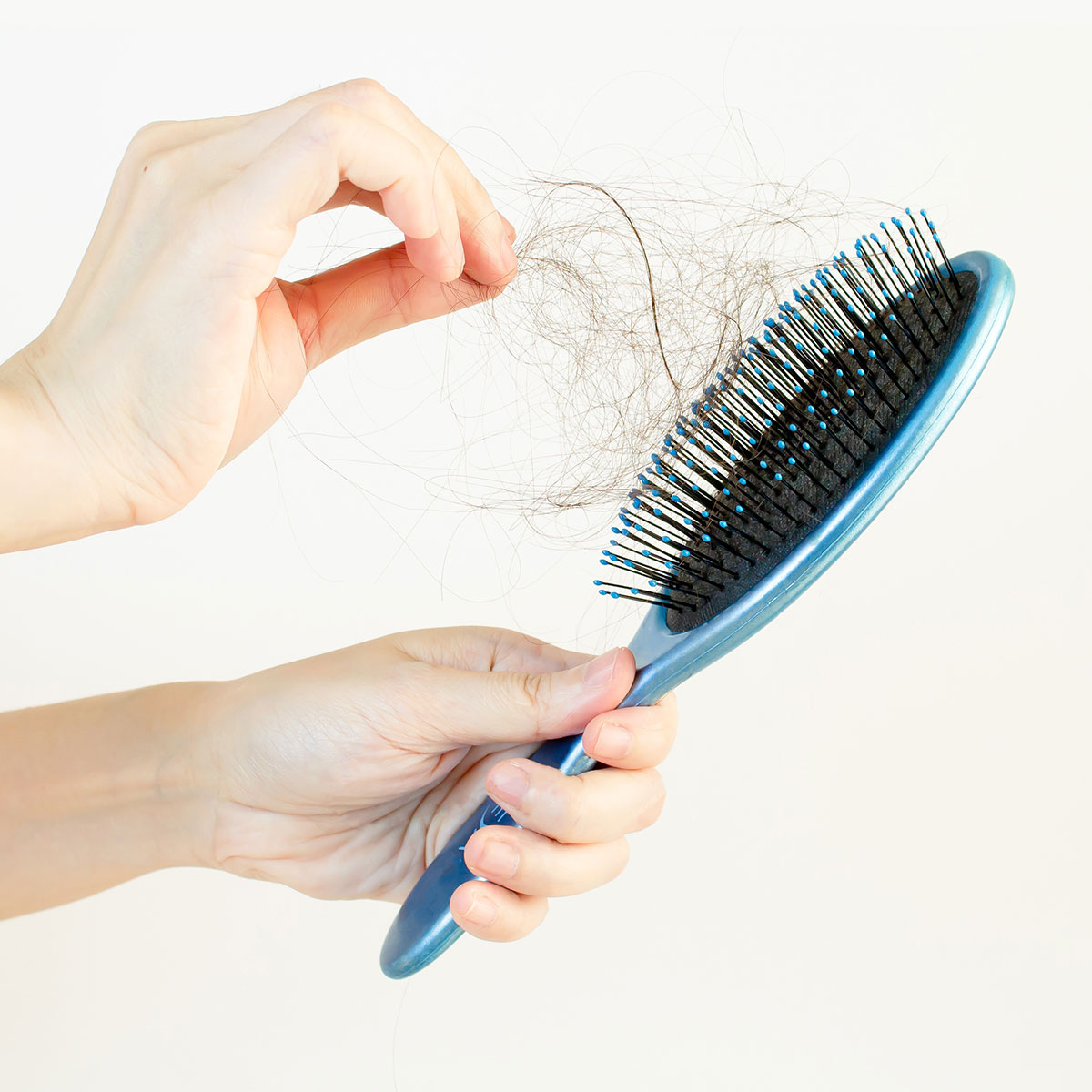 woman picking hair clumps out of blue hairbrush