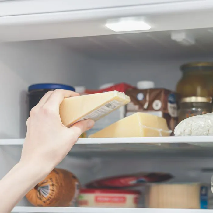 hand reaching for cheese wedge in the fridge