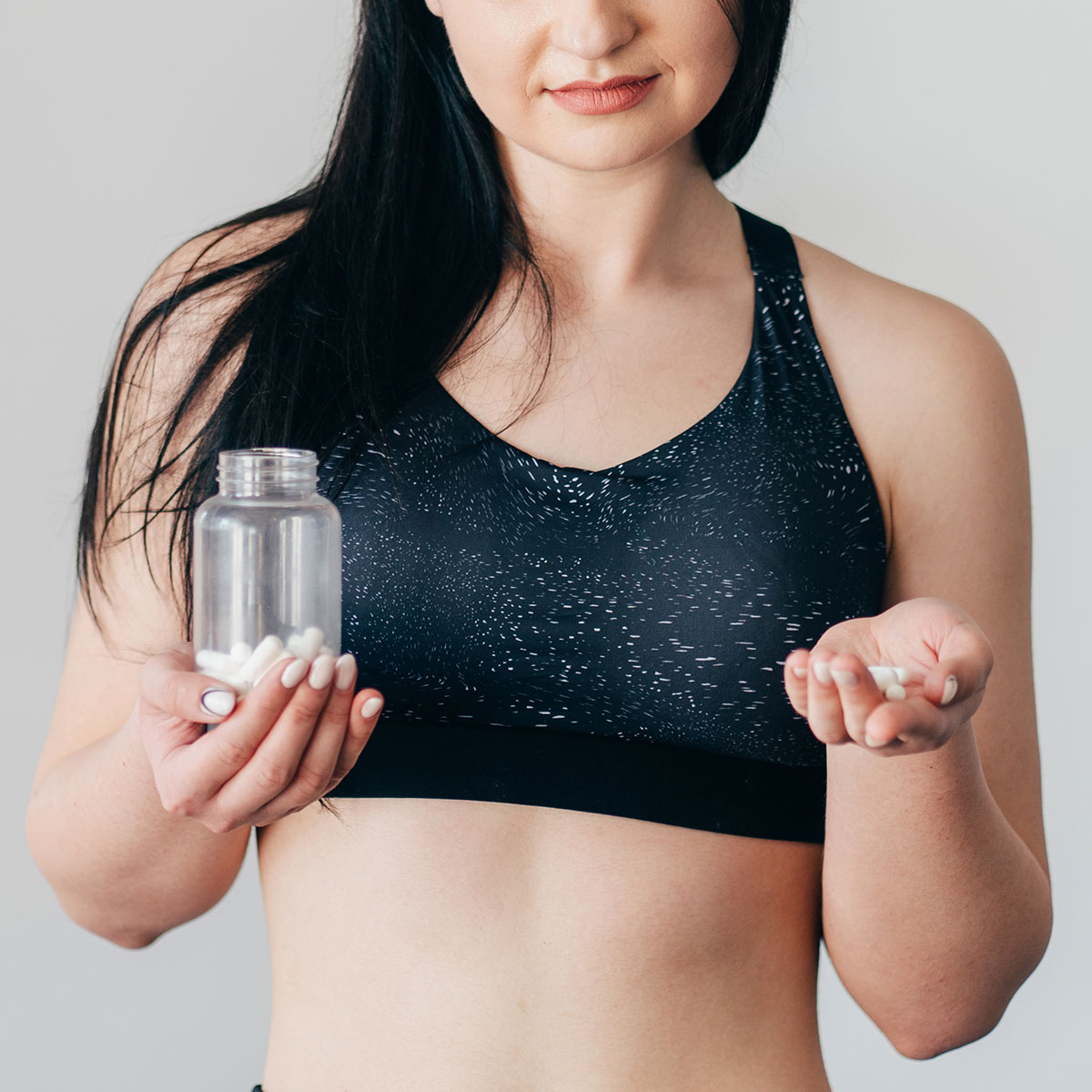 fit woman black sports bra holding jar of supplements open hand