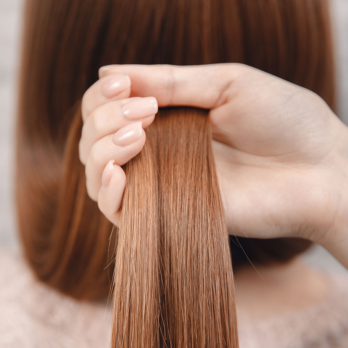 woman holding smooth shiny section of hair in hand