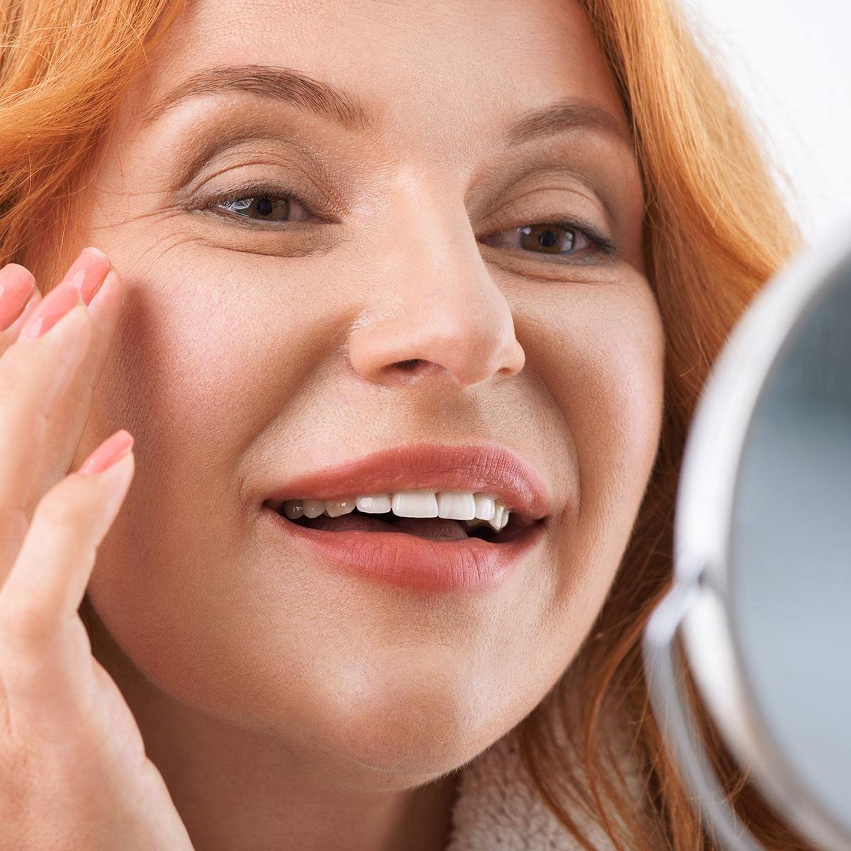 mature redhead woman smiling in mirror touching skin
