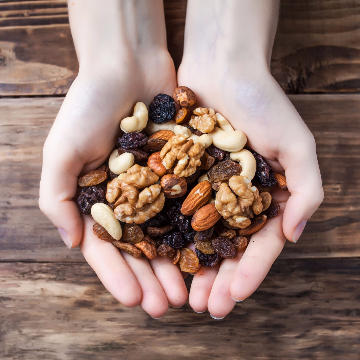hands holding mixed nuts dried fruits wooden background