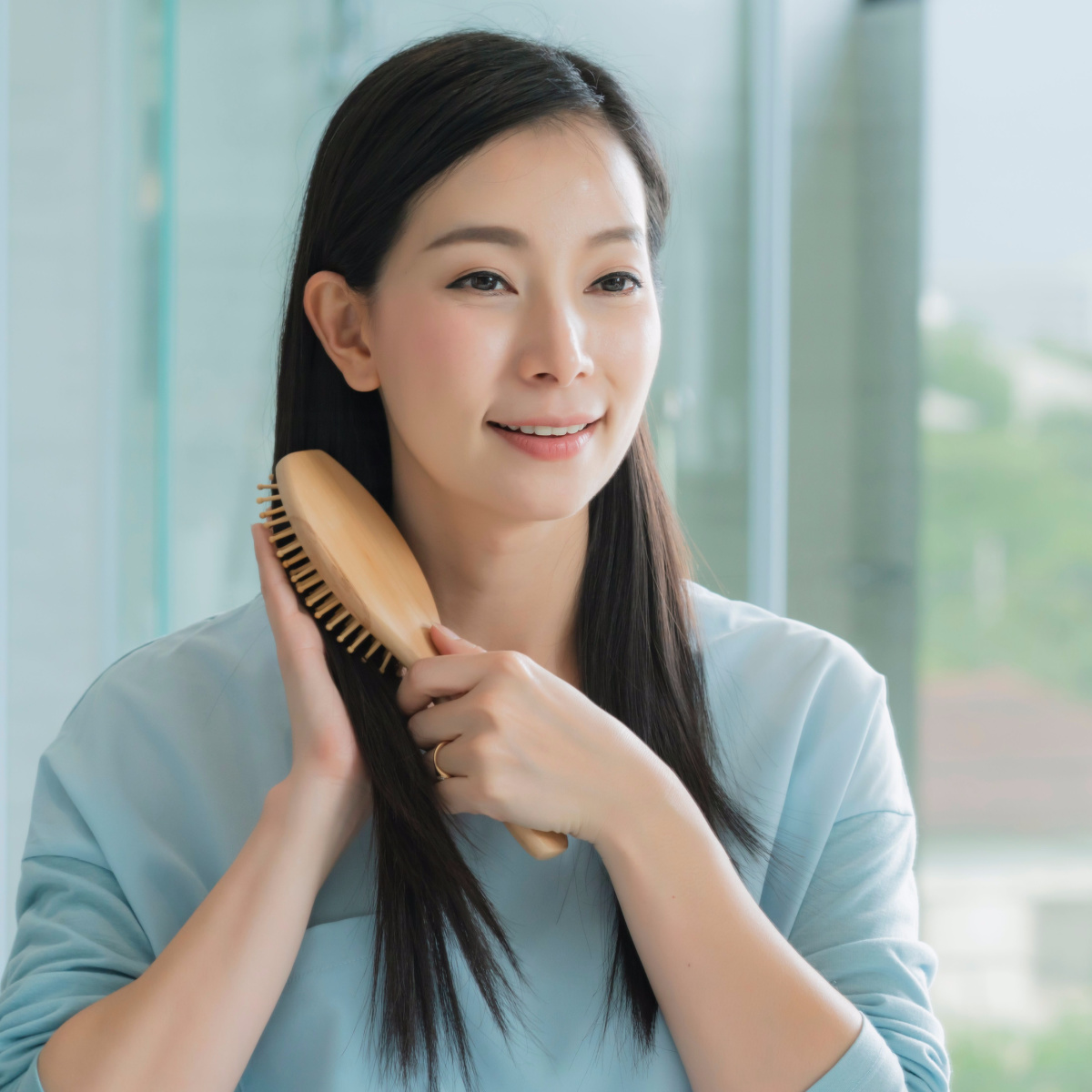 woman brushing long dark straight hair while looking in the mirror