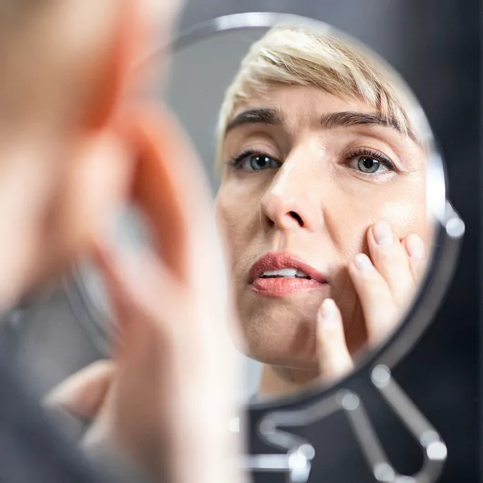 "Woman checking her wrinkles in a mirror"
