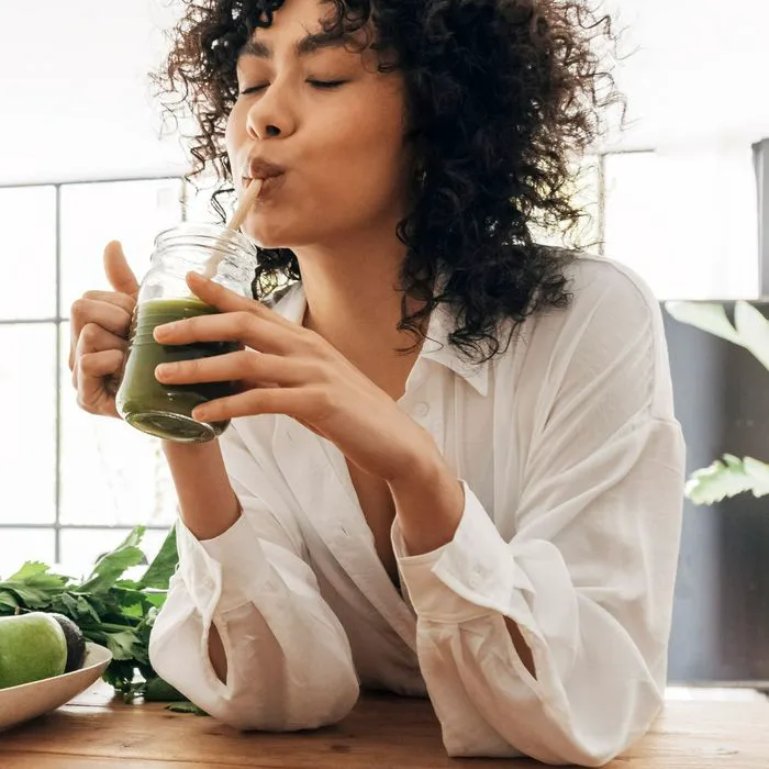 woman drinking green juice in kitchen