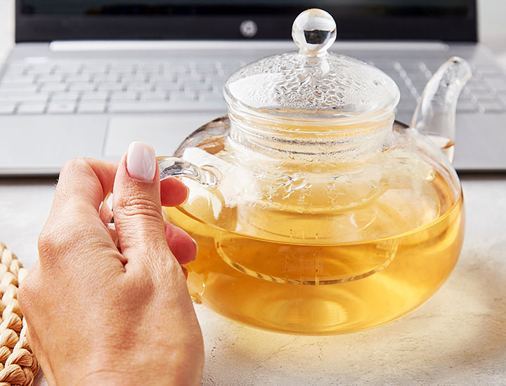 woman holding a glass teapot in front of laptop