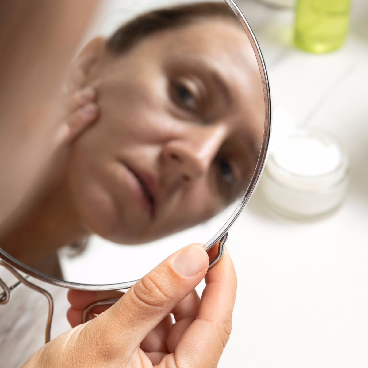 woman examining sun sagging skin in mirror handheld