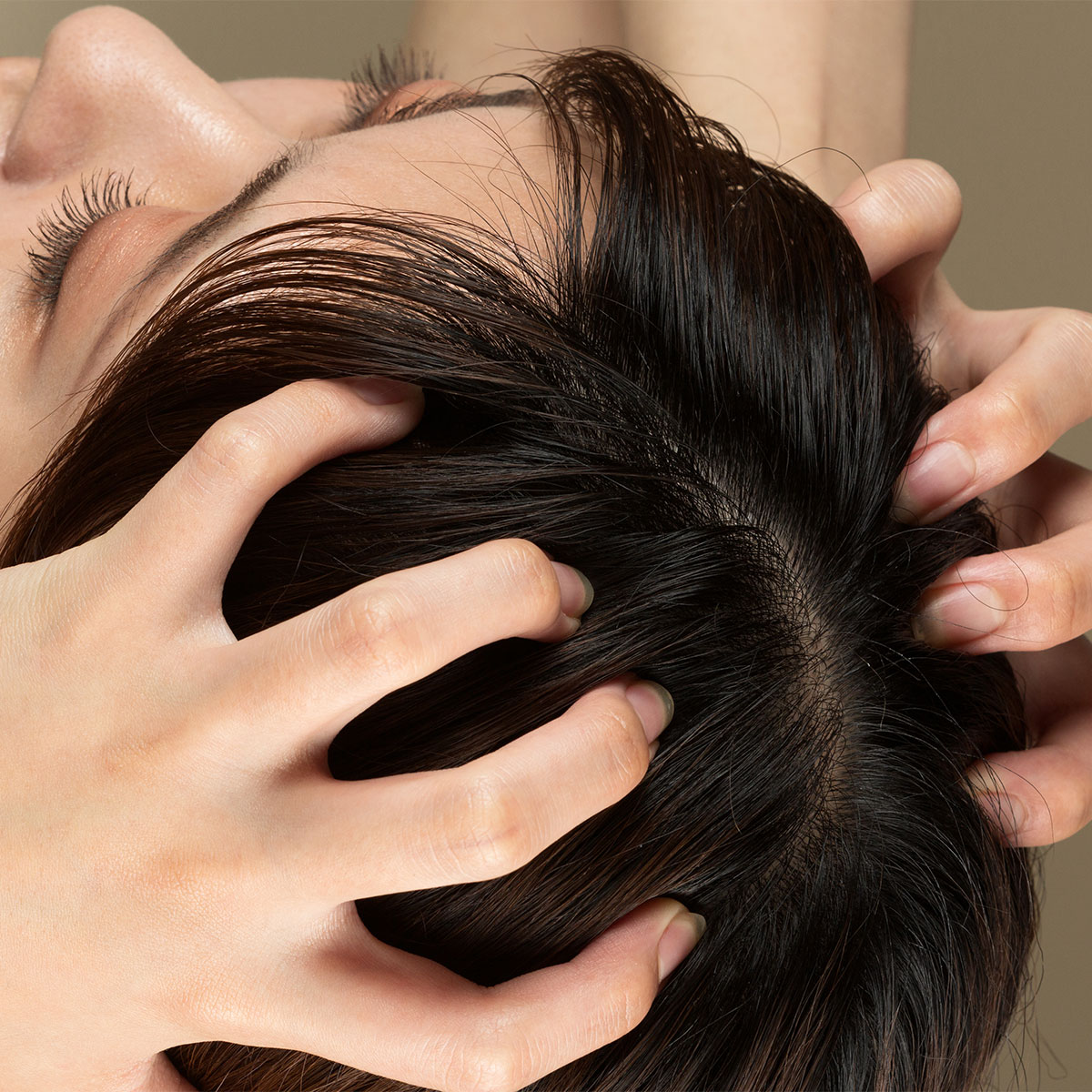 woman massaging scalp with hands nails scratching brown hair