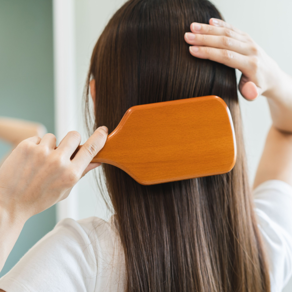 woman holding wooden brush up to straight brown hair