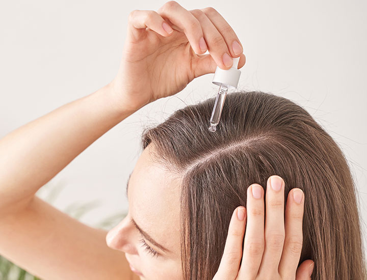 young woman applying scalp oil to hair center part