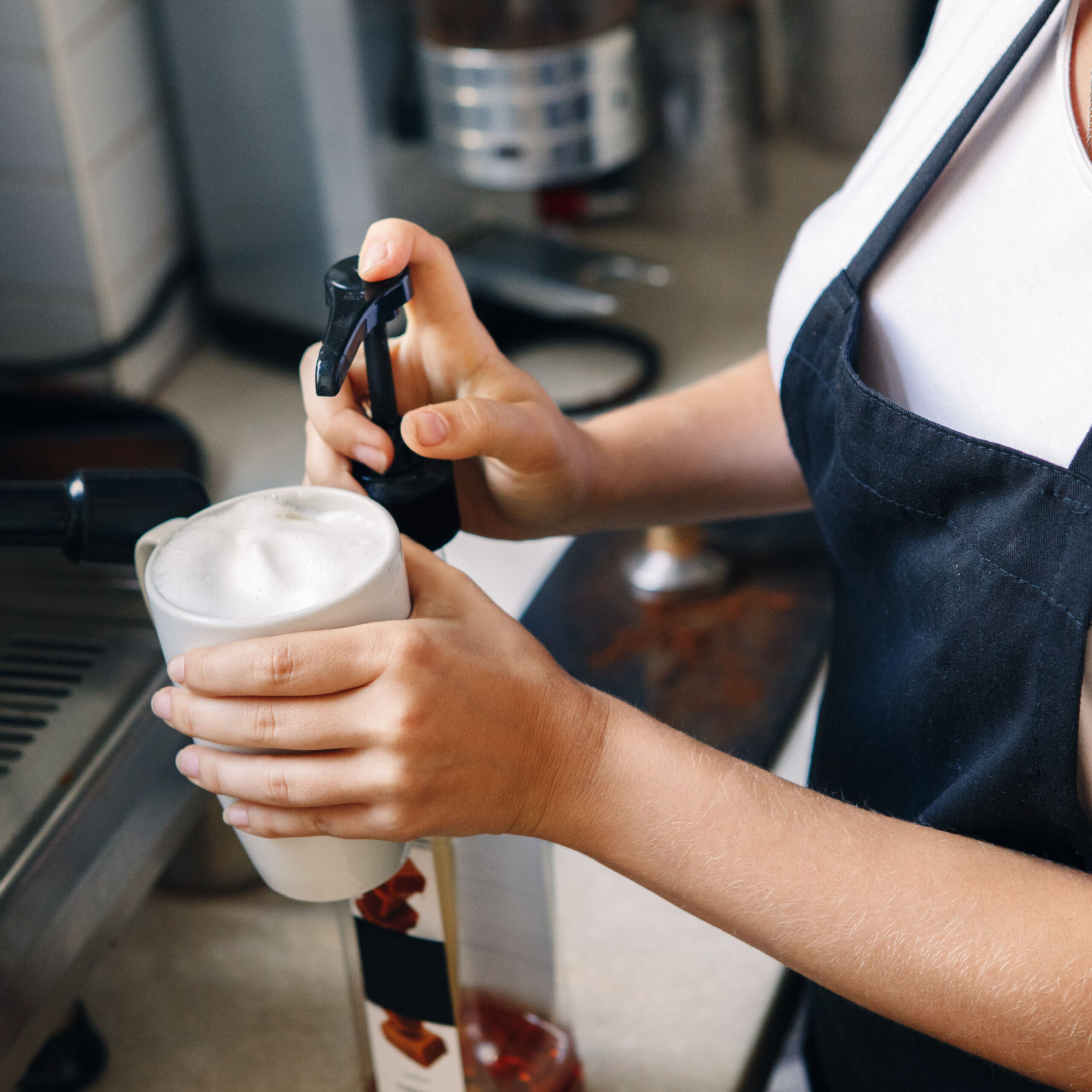 barista adding pump of syrup to coffee cup
