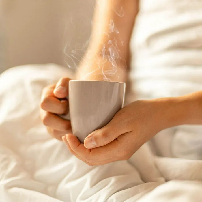 Woman enjoying a hot cup of tea in bed.