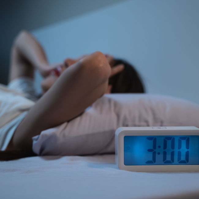 woman struggling to sleep while alarm clock says 3 AM