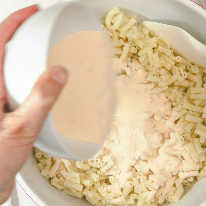 person adding cheese powder to macaroni