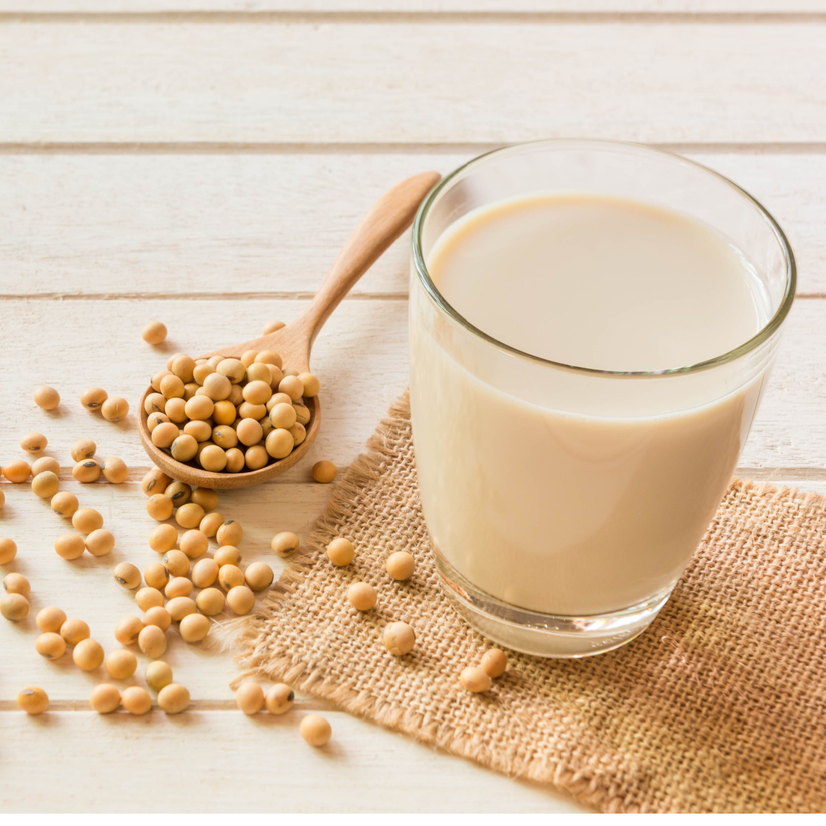 glass of soy milk surrounded by soy beans on wooden board