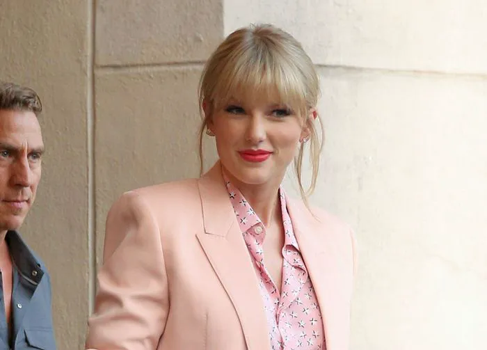 Taylor Swift in a pink jacket and sparkly silver shorts.