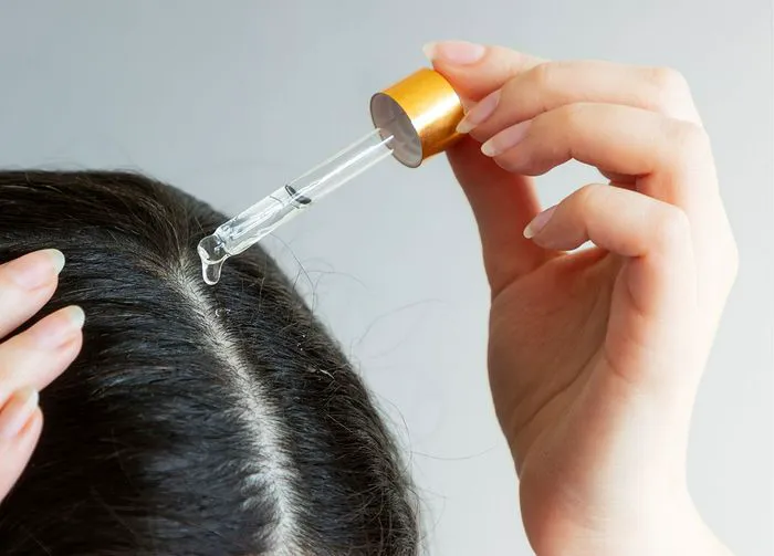 Dark-haired woman massaging hair oil into scalp.