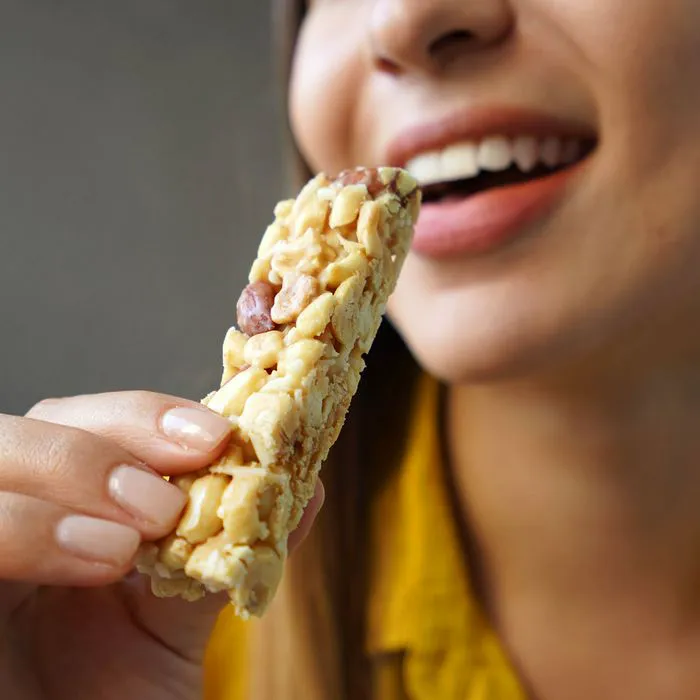"Woman smiling while eating a granola bar"