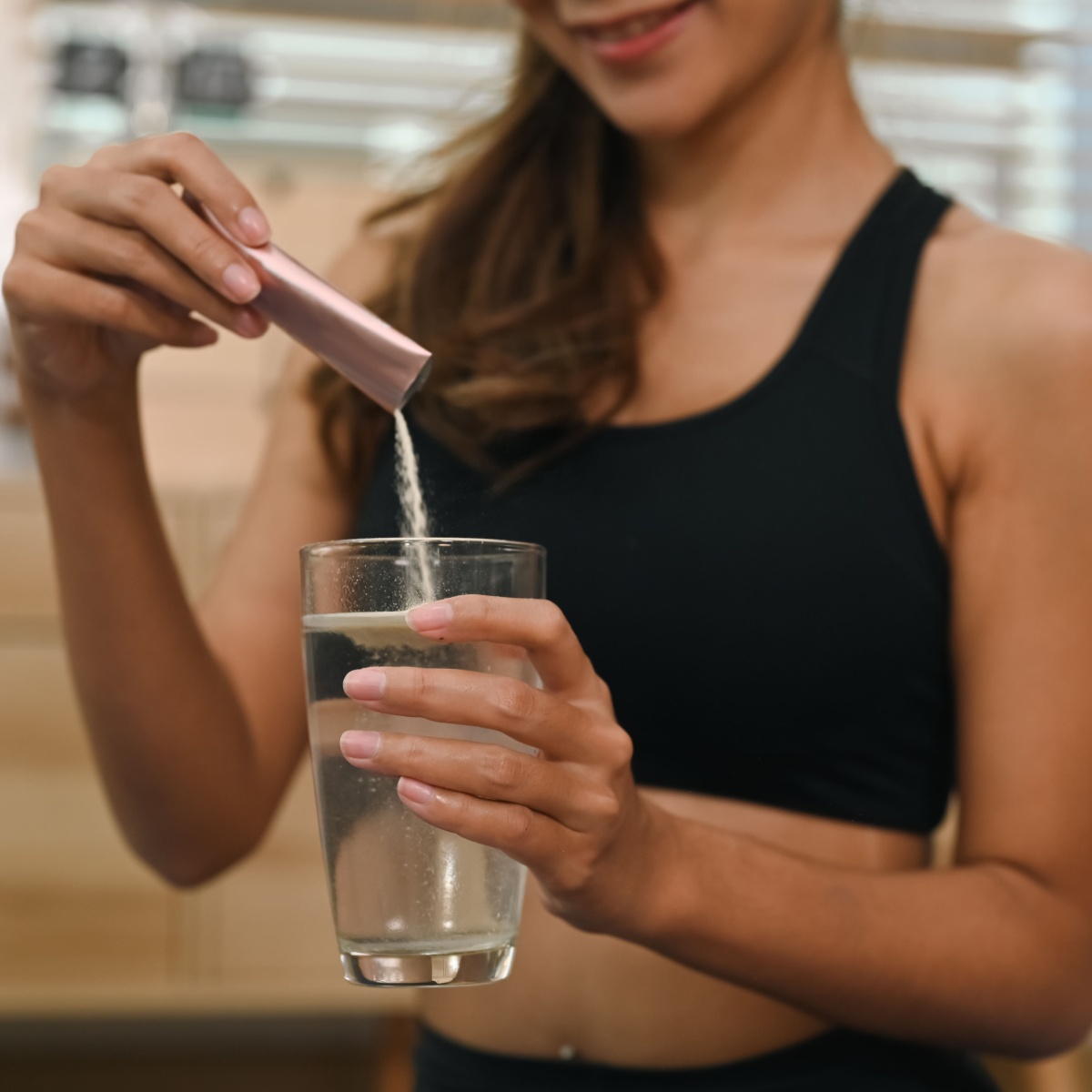 woman pouring supplement in glass of water