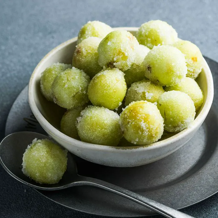 Bowl of frozen green grapes with a spoon, refreshing snack option.