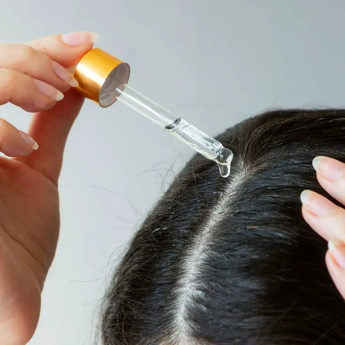 "Woman using a pipette with a cosmetic product near hair parting"