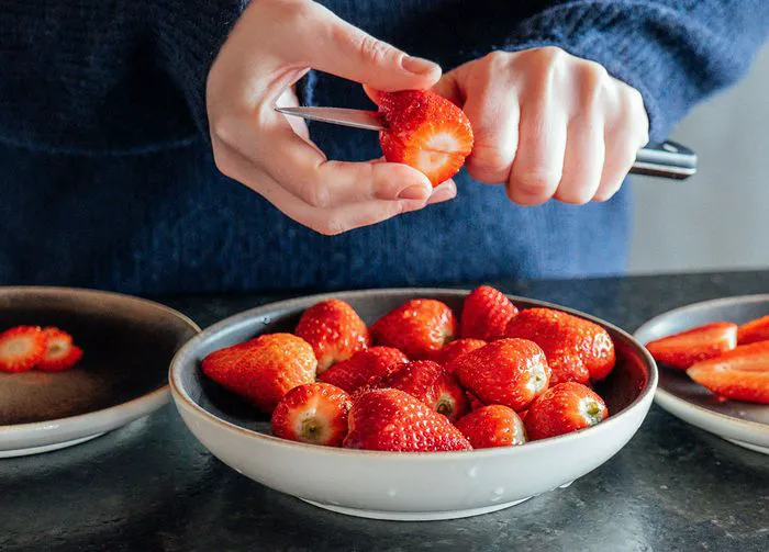 hands cut fresh strawberries and put in a plate