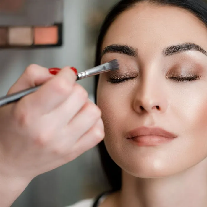 Makeup artist applying eyeshadow to a client's eyelid.