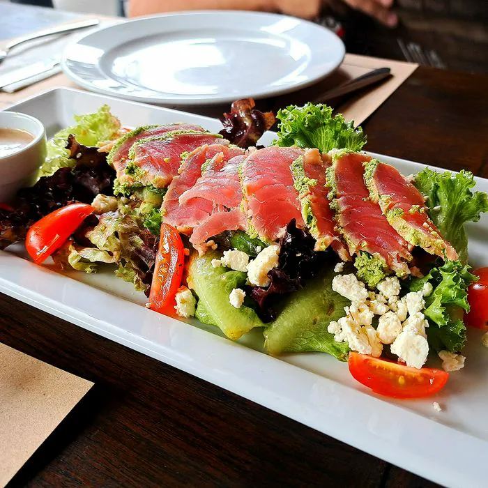 Sliced tuna steak served with green salad and sauce on a plate.