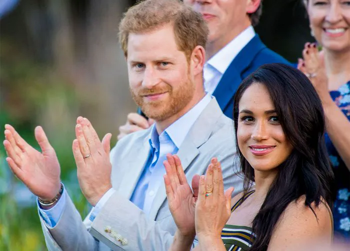 Meghan Markle and Prince Harry applauding at a public event.
