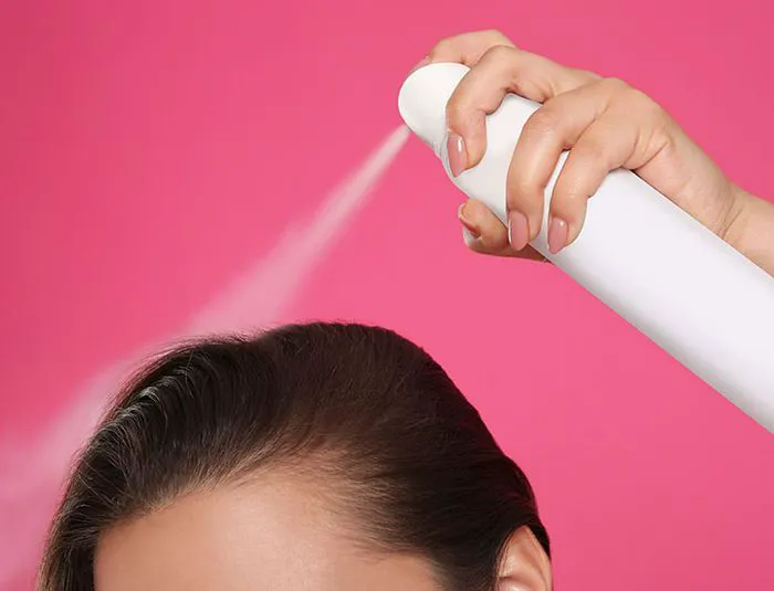 Pink background with dry shampoo bottle and spray.
