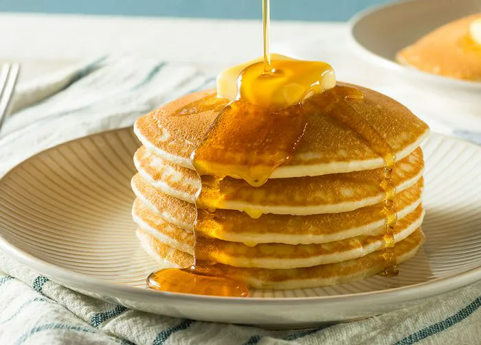 Stack of fluffy pancakes topped with butter and syrup.