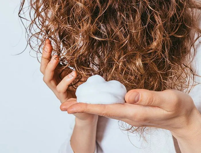 Person applying hair mousse with hands.