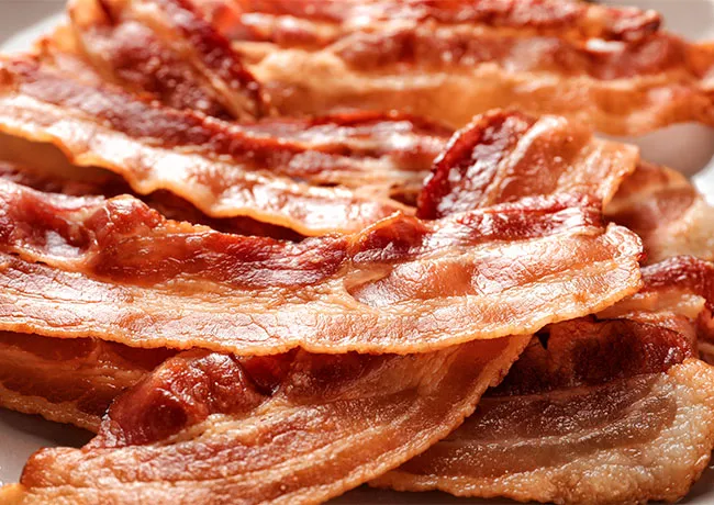 Plate of crispy bacon arranged on a white dish.