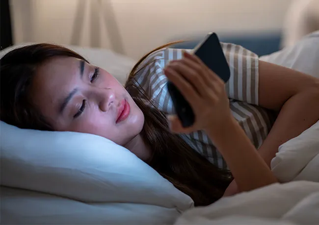 Woman lying in bed, using her phone and looking concerned.