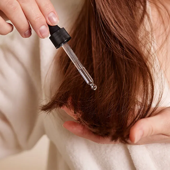 Woman applying hair care oil to her auburn hair.