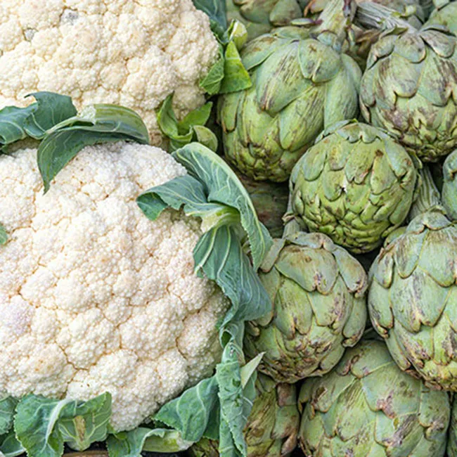 Fresh artichokes and cauliflower displayed at a farm stand.