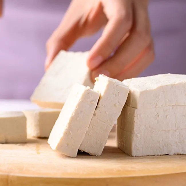 Chopping tofu on a wooden cutting board for a healthy meal.