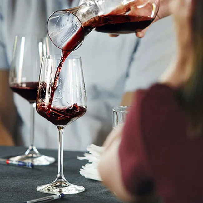 Pouring a glass of red wine at a dining table setting.