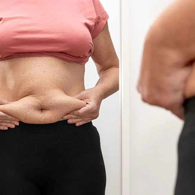 Woman examining her excess body fat in a mirror.