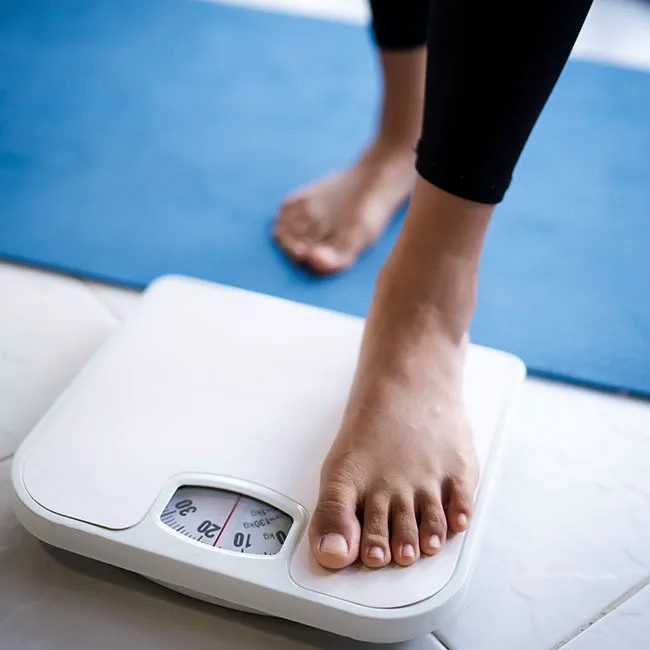 "Woman stepping on a scale to check weight"