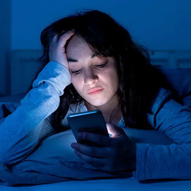 Young woman checking her phone while in bed.