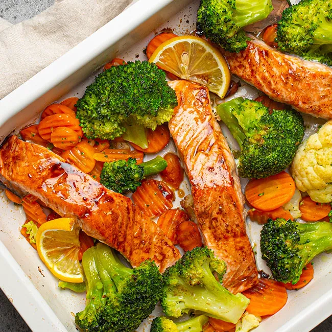 Roasted salmon fillet in a pan with colorful vegetables.