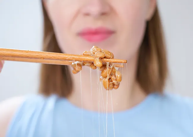 Woman using chopsticks to pick up natto dish.