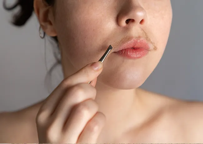 Young woman using tweezers to remove facial hair with focus.