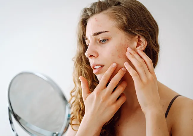 Young woman inspecting her skin in the mirror for blemishes.