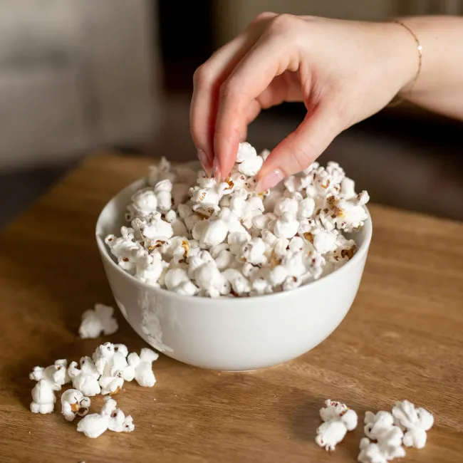 Hand reaching for fresh popcorn in a bowl.