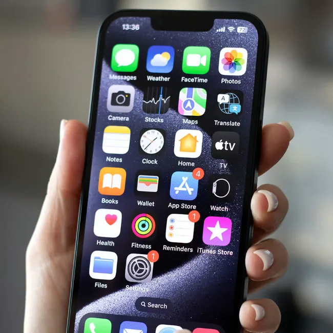 Woman holding iPhone with default apps, highlighting user interface.